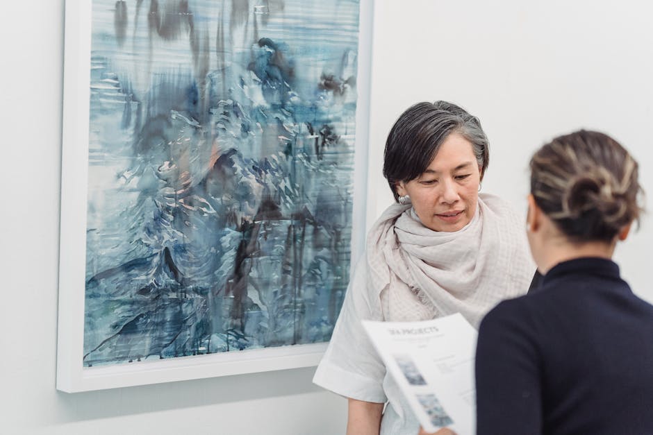 Two women discussing an abstract painting in a gallery setting, engaging in conversation.